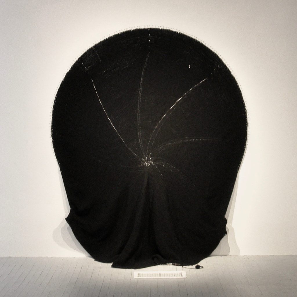 Diane Dubeau Tricot circulaire de laine noire accroché au mur
